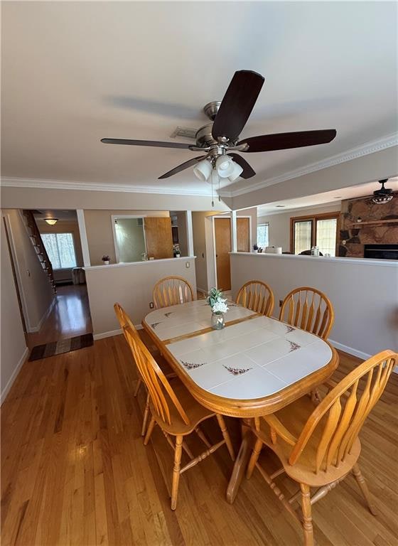 dining room featuring baseboards, light wood-type flooring, a fireplace, and crown molding