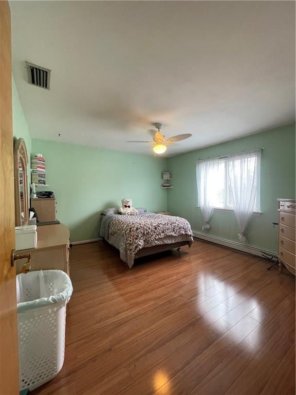 bedroom featuring a baseboard heating unit, visible vents, baseboards, and wood finished floors