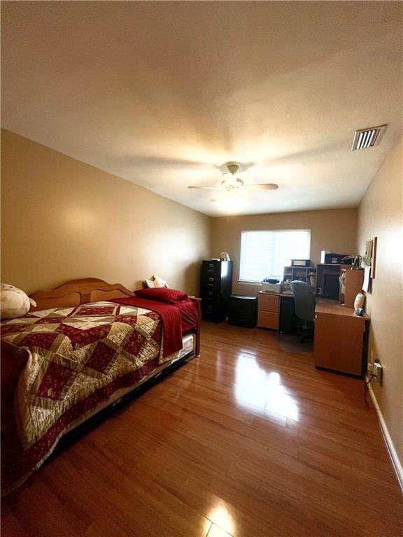 bedroom with a ceiling fan, visible vents, baseboards, and wood finished floors