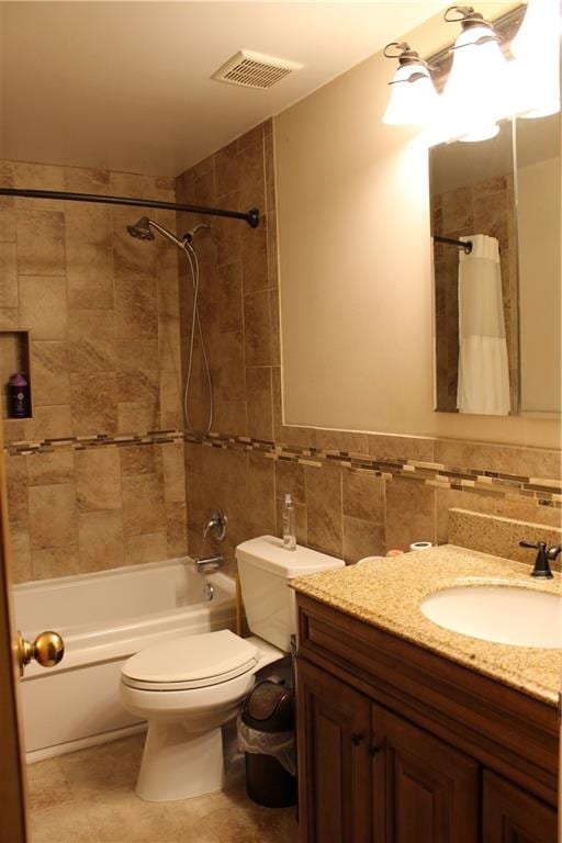 bathroom with toilet, vanity, visible vents, tile walls, and shower / bath combo