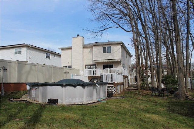 rear view of house featuring fence, a lawn, a wooden deck, a covered pool, and a chimney