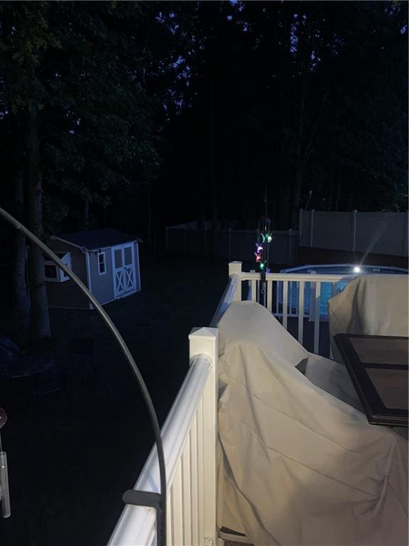 pool at night featuring a storage shed, an outbuilding, a fenced backyard, and a fenced in pool