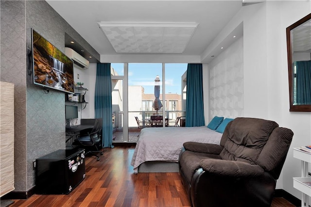 bedroom with an accent wall, a wall mounted air conditioner, a tray ceiling, expansive windows, and wood finished floors