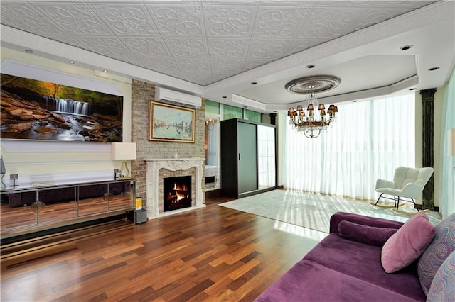 living room with an ornate ceiling, wood finished floors, a wall unit AC, a brick fireplace, and a chandelier