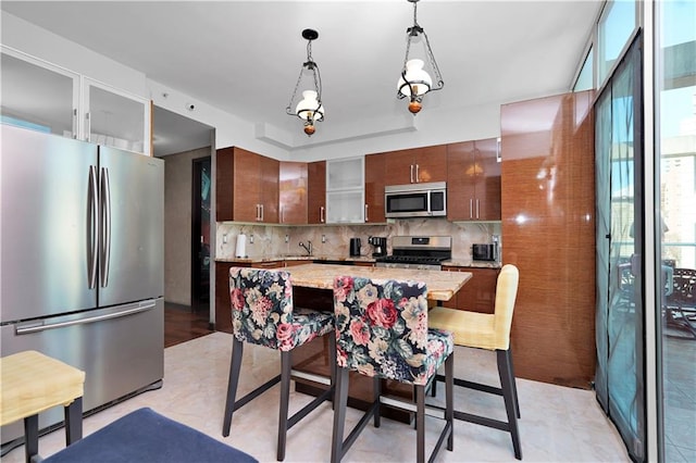 kitchen with pendant lighting, a sink, appliances with stainless steel finishes, decorative backsplash, and light stone countertops