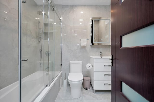 full bath featuring vanity, tile walls, toilet, and bath / shower combo with glass door