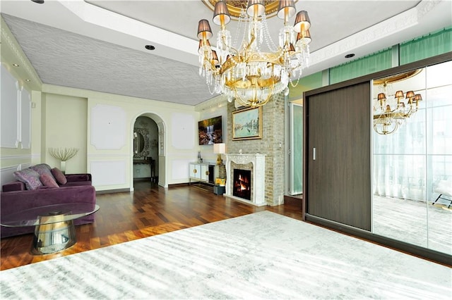 living area with arched walkways, a notable chandelier, wood finished floors, and a fireplace