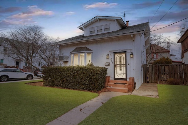 bungalow-style home with stucco siding, fence, and a yard