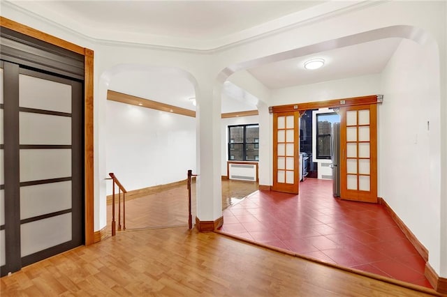 unfurnished room with arched walkways, french doors, baseboards, and wood finished floors