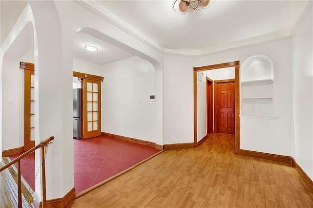 hall featuring arched walkways, ornamental molding, light wood-type flooring, and baseboards