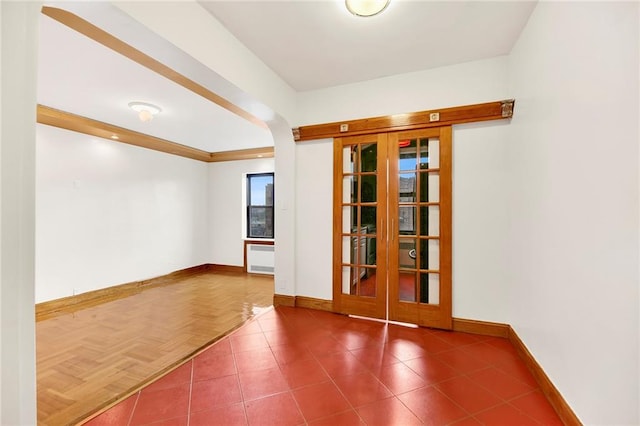 tiled empty room with arched walkways, radiator, and baseboards