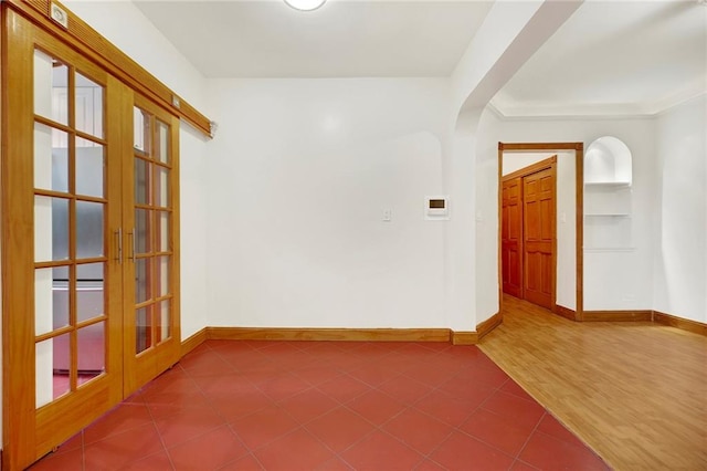 empty room with arched walkways, tile patterned flooring, built in features, baseboards, and french doors