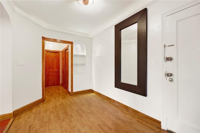 corridor with built in features, arched walkways, baseboards, and light wood finished floors