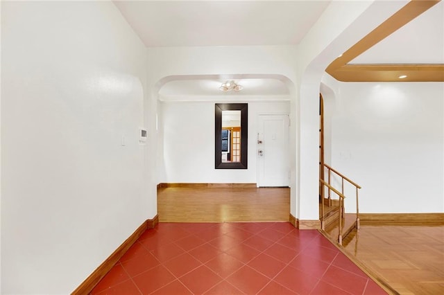 hall featuring dark tile patterned floors, arched walkways, and baseboards