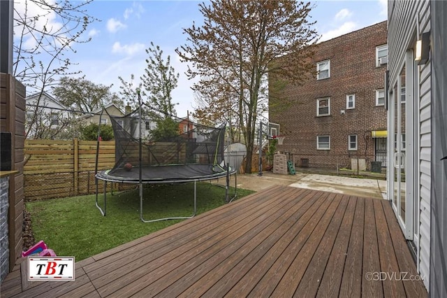 deck featuring a trampoline, a fenced backyard, and a yard