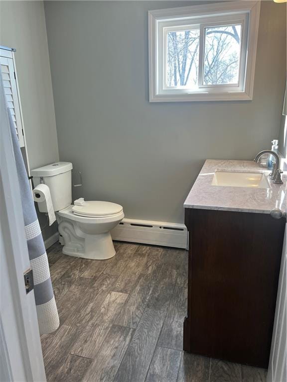 bathroom with toilet, wood finished floors, baseboards, baseboard heating, and vanity