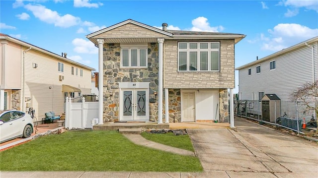 view of front of property with stone siding, french doors, a front yard, and fence