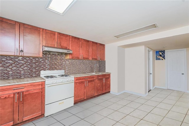 kitchen featuring white gas stove, under cabinet range hood, a sink, light countertops, and decorative backsplash