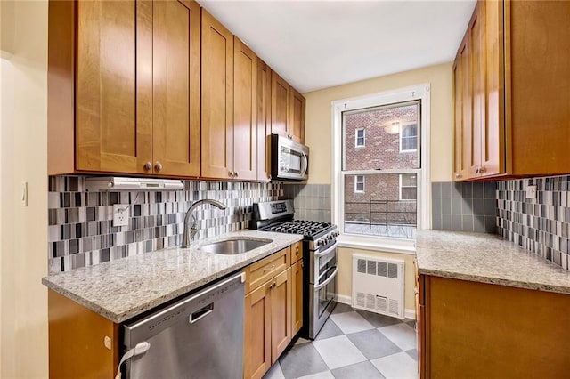 kitchen with radiator heating unit, appliances with stainless steel finishes, light stone counters, and a sink