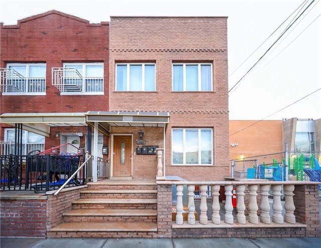 townhome / multi-family property with fence, a porch, and brick siding