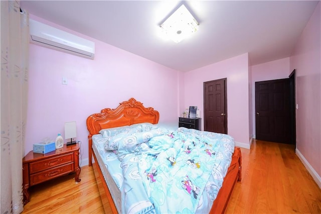 bedroom featuring light wood-style flooring, baseboards, and an AC wall unit