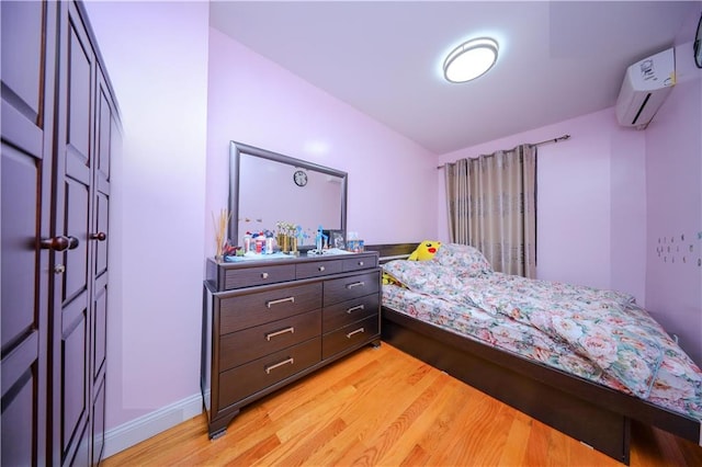 bedroom with light wood finished floors, baseboards, and a wall mounted AC