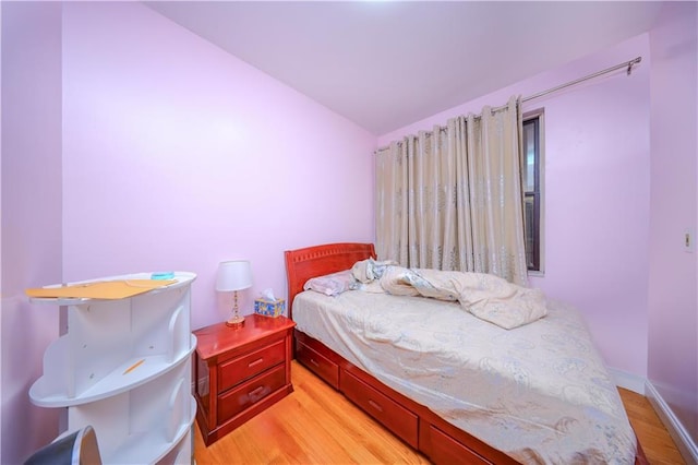 bedroom featuring light wood-style floors, lofted ceiling, and baseboards