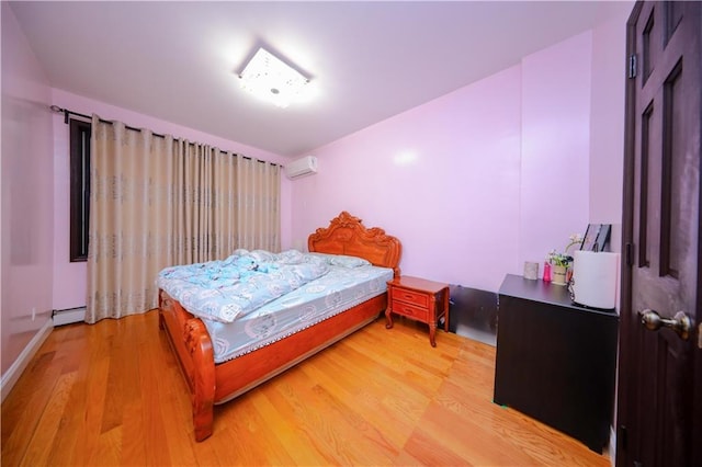 bedroom with a wall unit AC, light wood finished floors, and a baseboard radiator