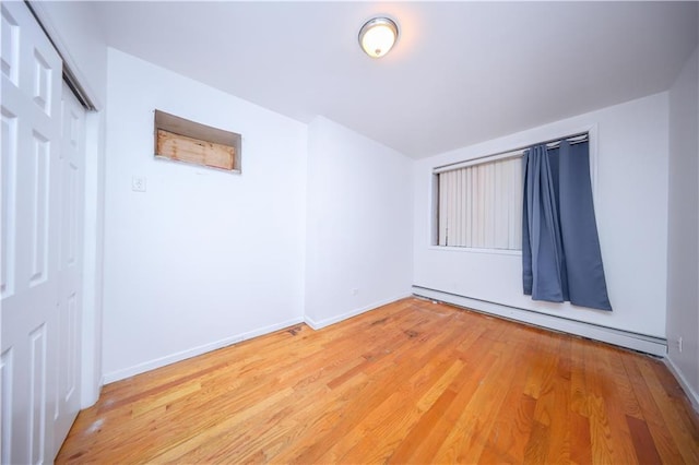 unfurnished room with baseboards, light wood finished floors, and baseboard heating