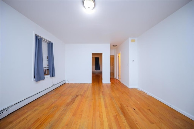 empty room featuring light wood-type flooring, baseboards, and baseboard heating