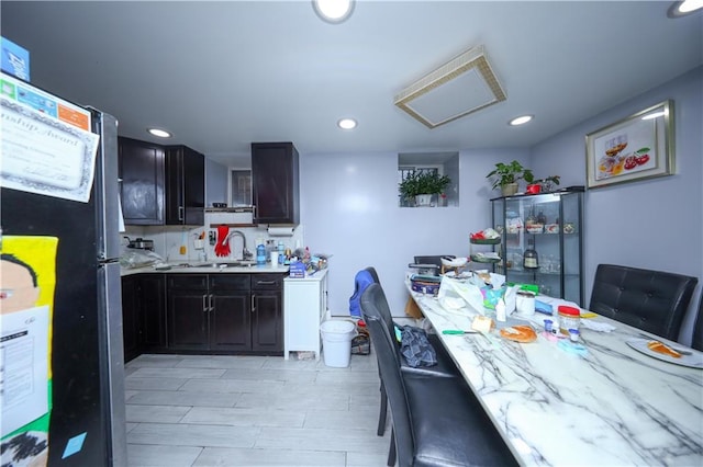 kitchen with dark cabinets, a sink, freestanding refrigerator, and recessed lighting