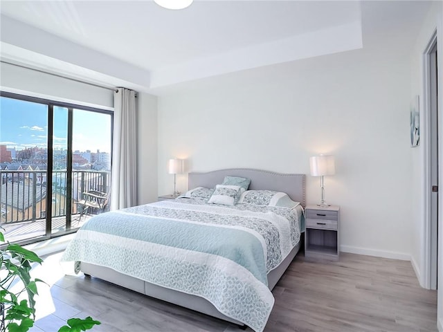 bedroom featuring access to outside, a view of city, baseboards, and wood finished floors