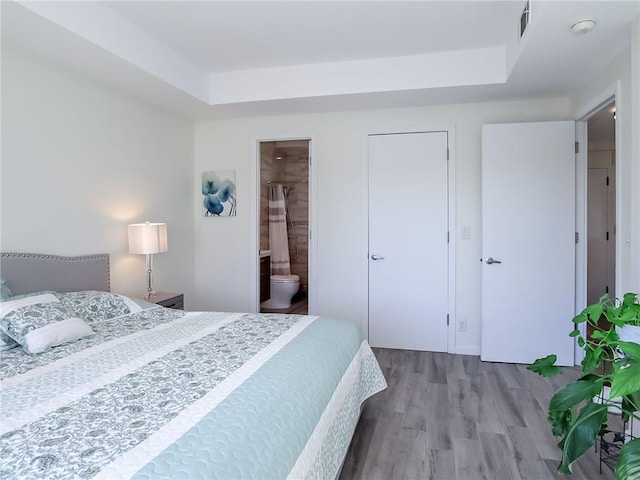 bedroom with a tray ceiling, wood finished floors, and ensuite bathroom