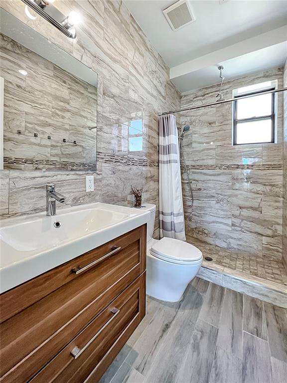 full bathroom featuring tile walls, tasteful backsplash, toilet, vanity, and tiled shower