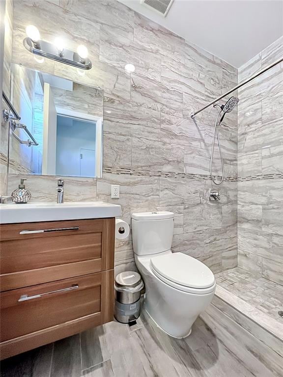 full bath with toilet, visible vents, vanity, tile walls, and a tile shower