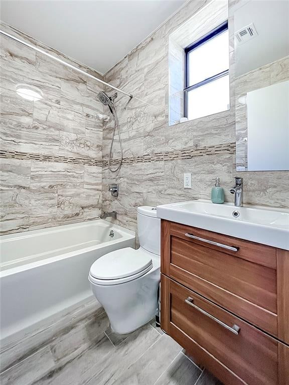 bathroom featuring tile walls, visible vents, toilet, washtub / shower combination, and vanity