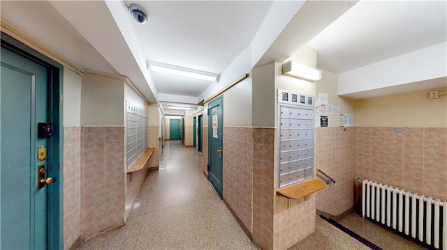 hall with radiator, a wainscoted wall, mail area, and tile walls