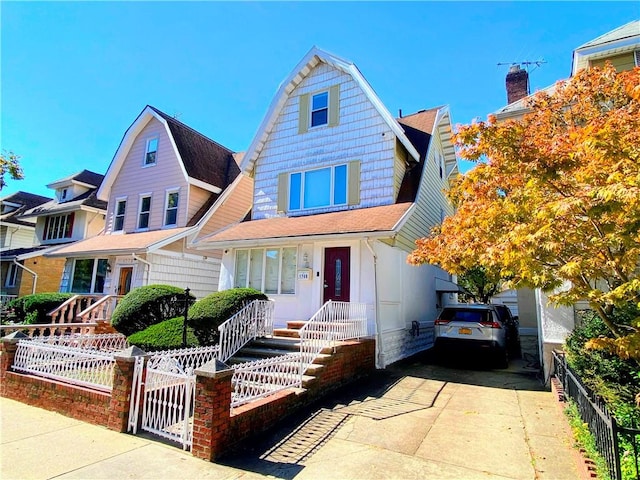 view of front of house with concrete driveway, a shingled roof, a fenced front yard, and a gambrel roof