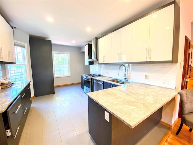 kitchen featuring tasteful backsplash, appliances with stainless steel finishes, a peninsula, wall chimney range hood, and a sink