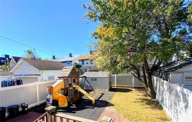 view of yard featuring a playground, an outdoor structure, a fenced backyard, and a storage unit