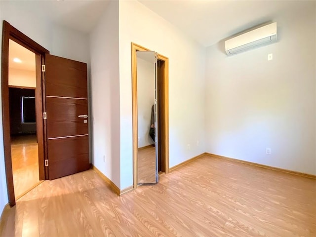 hall featuring a wall unit AC, light wood finished floors, and baseboards