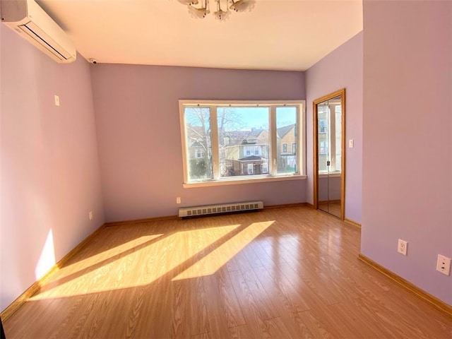 empty room featuring an AC wall unit, baseboard heating, wood finished floors, a chandelier, and baseboards