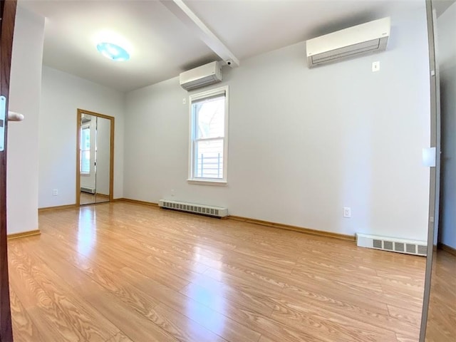 spare room featuring a wall mounted AC, light wood-type flooring, and baseboards