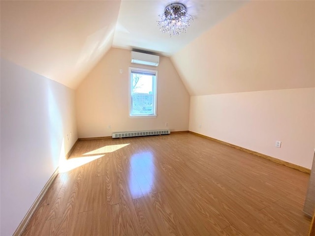 additional living space with an AC wall unit, a baseboard radiator, wood finished floors, lofted ceiling, and baseboards