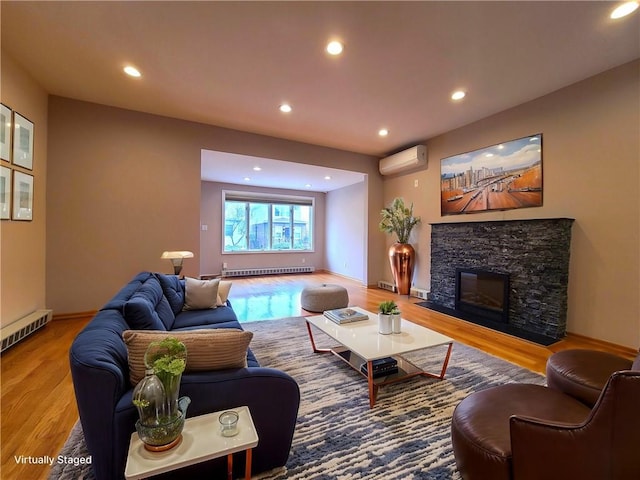 living area with a baseboard radiator, a wall unit AC, wood finished floors, recessed lighting, and a stone fireplace