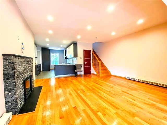 living room featuring a fireplace, recessed lighting, a baseboard heating unit, light wood-type flooring, and stairs