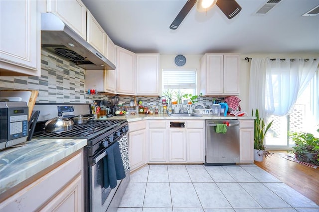 kitchen featuring ceiling fan, appliances with stainless steel finishes, light countertops, decorative backsplash, and under cabinet range hood