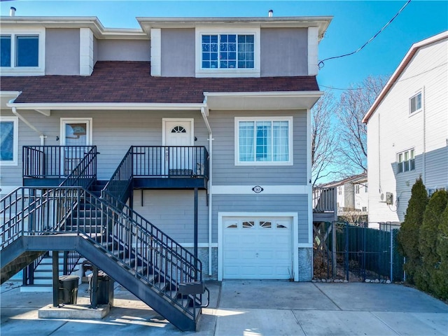 view of property with driveway, roof with shingles, stairway, fence, and an attached garage