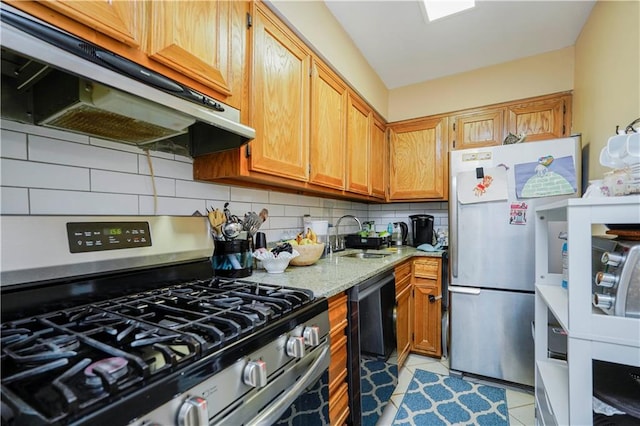 kitchen featuring under cabinet range hood, a sink, tasteful backsplash, appliances with stainless steel finishes, and light stone countertops