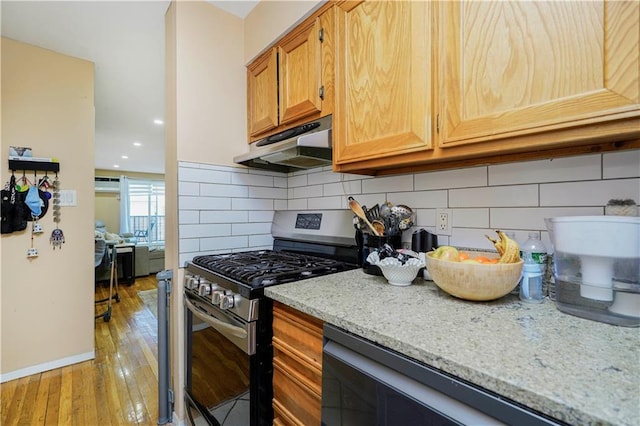 kitchen featuring light wood-style flooring, under cabinet range hood, light stone counters, tasteful backsplash, and gas range